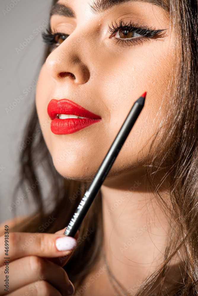 Makeup artist applies red lipstick . Beautiful woman face. Hand of make-up master, painting lips of young beauty model girl . Make up in process