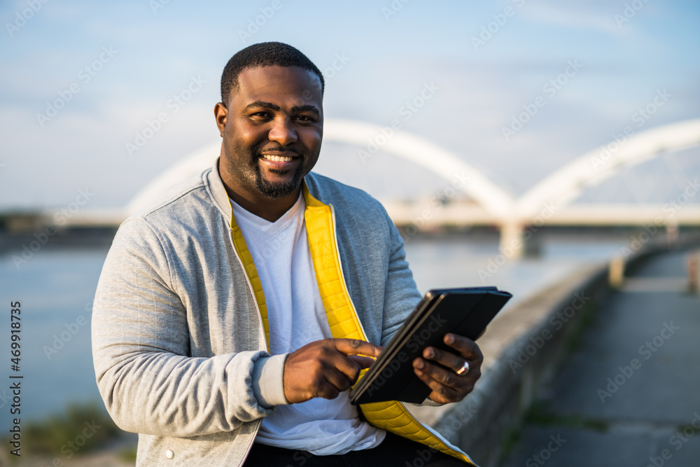 Modern black man using digital tablet while sitting by a river.