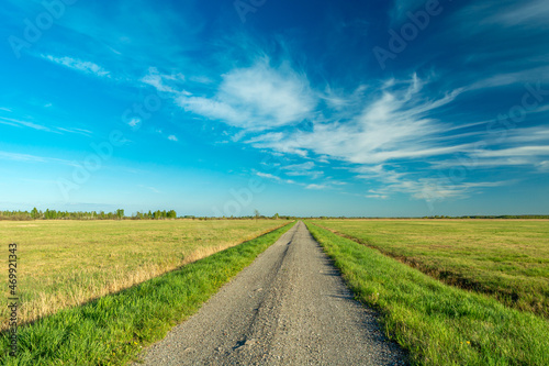 Gravel road through meadows and blue sky