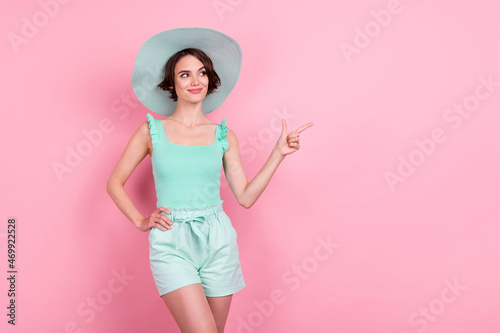 Photo of sweet brown hairdo young lady point look empty space wear hat teal top shorts isolated on pink color background © deagreez