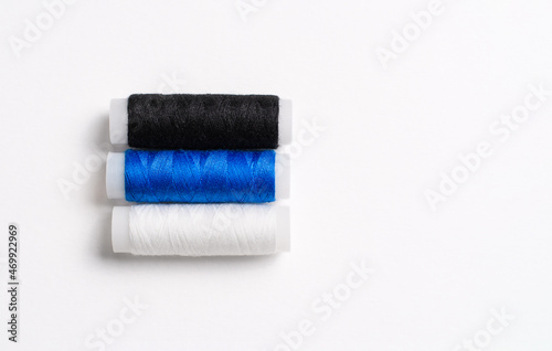 Three spools of thread for sewing are stacked in the form of the flag of Estonia on a white background. There is a free empty space.