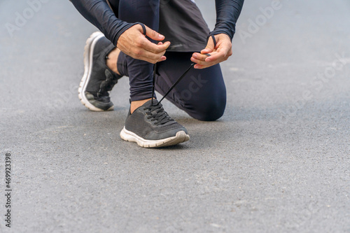 Hands of jogger young man tying shoelace on the road while workout in park. Healthy exercise comfortable sport shoes concept.