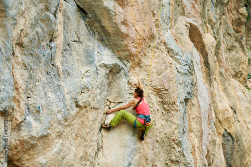 Rear view climber woman climbing on beautiful rock wall, ready to making move up on challenging route