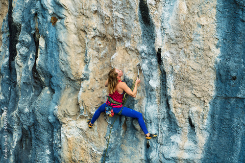 Athletic woman climbing on high beautiful rock cliff, feeling determined on challenge route