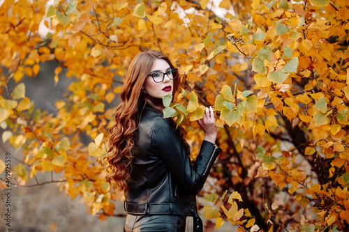 portrait of a beautiful young woman, wearing stylish glasses, looking at the camera. Happy, confident, smart young woman in autumn foliage