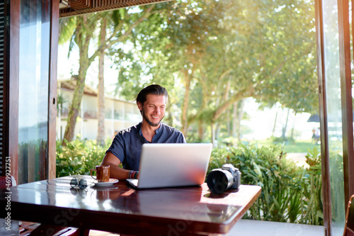 Freelance concept. Professional photographer. Young  bearded man using laptop while sitting on summer terrace. © luengo_ua