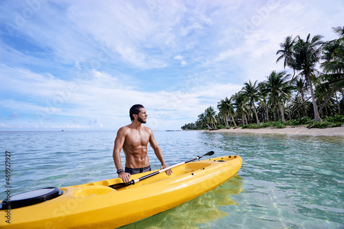 Young man with sea kayak on the tropical beach.