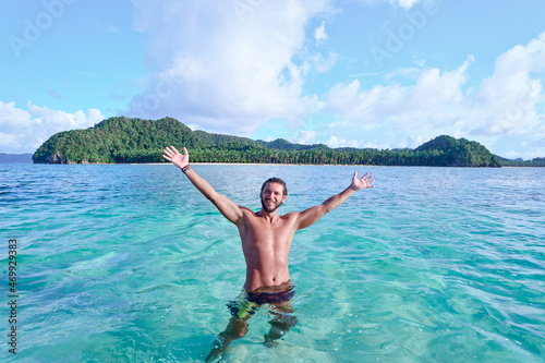 Vacation and freedom. Happy young man rising hands up bathing on tropical beach enjoying beautiful view.