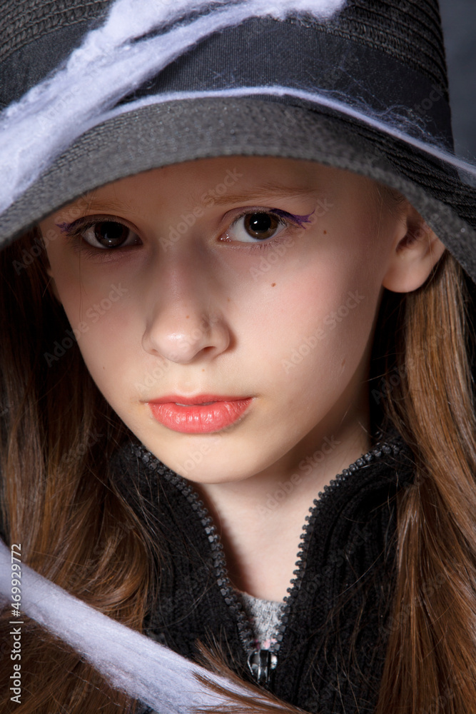 Little girl in a black hat on a halloween spider web.