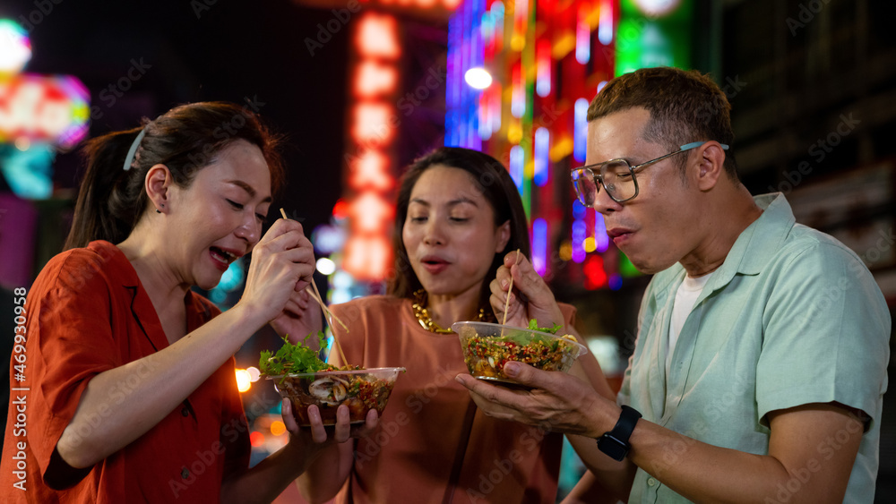 Group of Asian woman and LGBTQ people friends tourist enjoy eating traditional street food bbq seafood grilled squid with spicy sauce together at china town street night market in Bangkok, Thailand - obrazy, fototapety, plakaty 