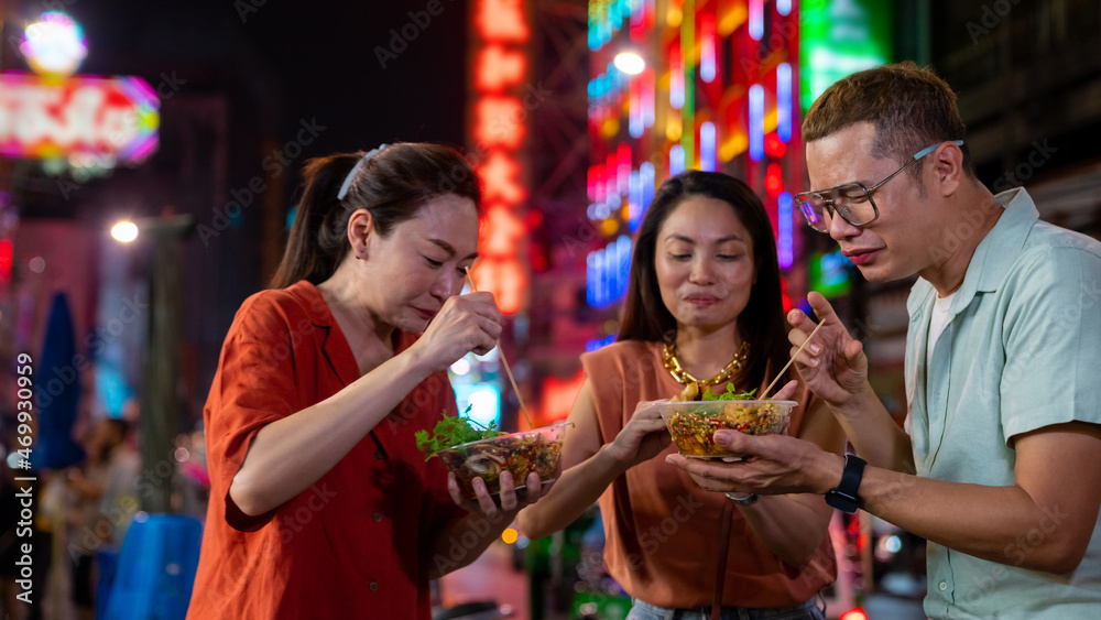 Fototapeta premium Group of Asian woman and LGBTQ people friends tourist enjoy eating traditional street food bbq seafood grilled squid with spicy sauce together at china town street night market in Bangkok, Thailand