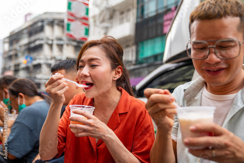 Photography Asian people tourist walking and eating traditional Thai dessert together at chinatown street market in Bangkok city, Thailand
