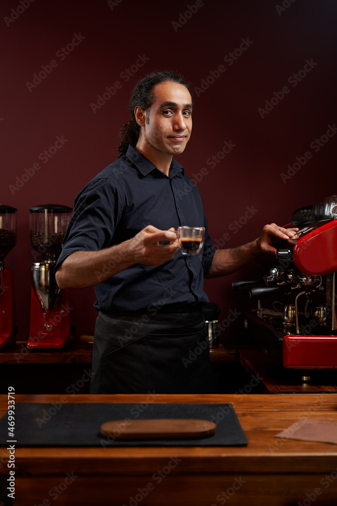 Portrait of a handsome barista in black shirt and apron at the bar of the modern cafe.