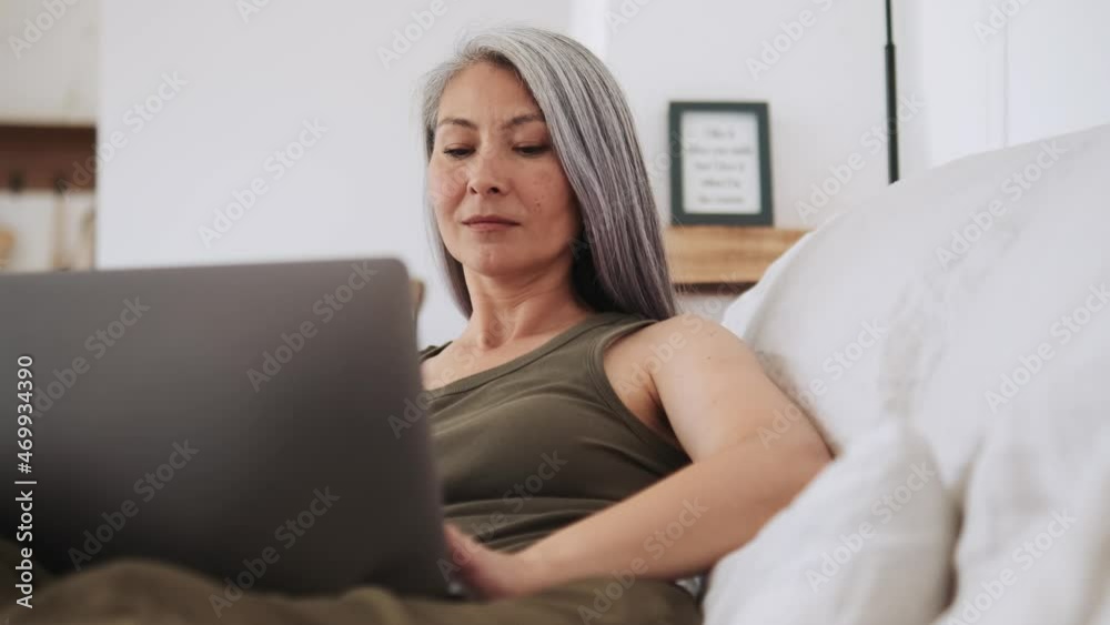Concentrated Asian woman typing at laptop at home