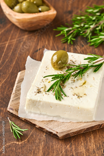 Cheese feta with rosemary, herbs, olives and olive oil on wooden cutting board on old wooden background. Traditional Greek homemade cheese. Selective focus.