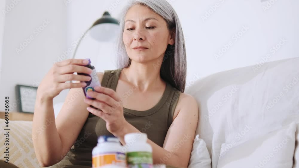 Concentrated Asian woman looking at the jar of medicines at home Concentrated Asian woman looking at the jar of medicines at home