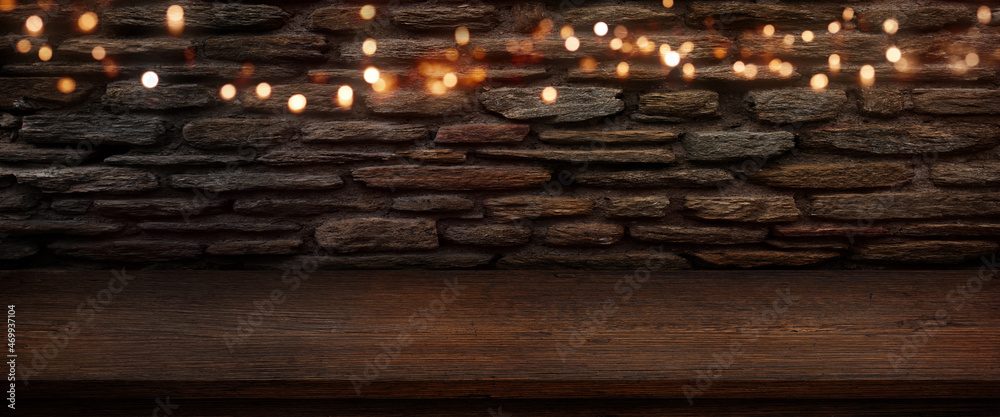 Iluminated old stonewall with golden bokeh and empty wooden. counter. Background for a restaurant and bar concept. Space for decorations. - obrazy, fototapety, plakaty 
