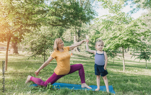 a sporty grandmother exercises with her granddaughter in a gym mat in the park. © Tatsiana