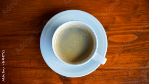 a cup of coffee on the white saucer. a morning coffee served on the wooden table from the top view. a shot of beverage object suitable for background or promotion.