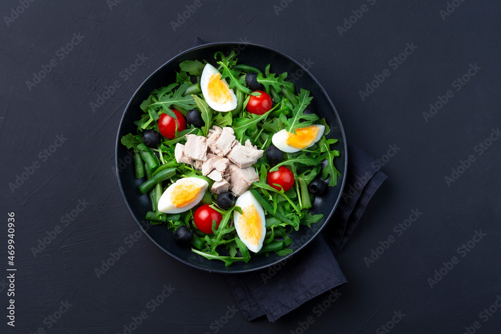 tasty tuna salad in a black bowl on black background