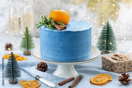 Christmas blue cake decorated with tangerine, cinnamom sticks on a blue background with a Christmas decoration or winter holidays pastry food concept.