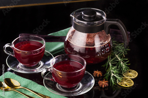 Fruit red tea with berries in glass teapot and two glass cups on black background