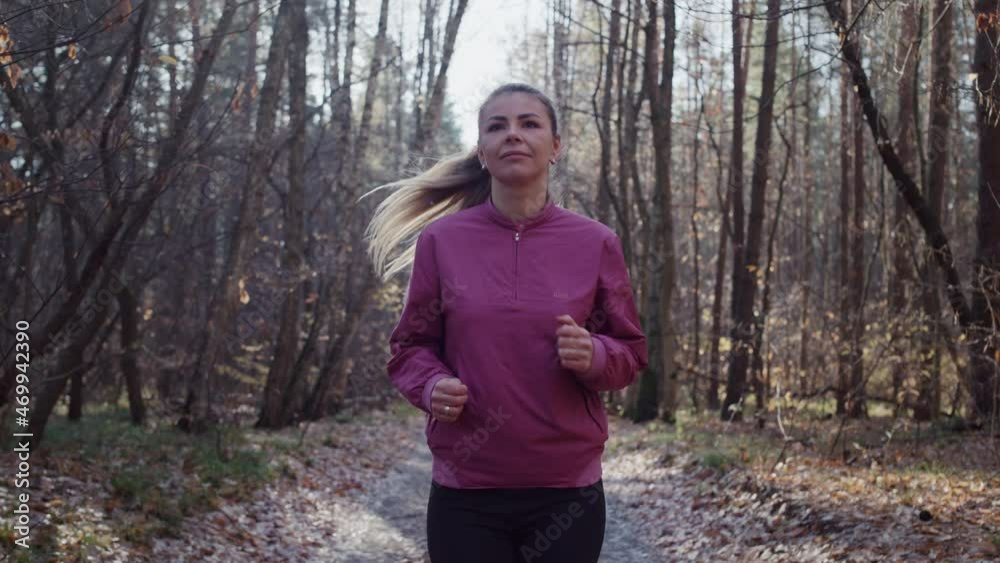Caucasian woman running on a path in the woods. The girl goes in for sports in nature in the autumn park, yellow leaves fall from the trees. Caucasian woman running on a path in the woods. The girl goes in for sports in nature in the autumn park, yellow leaves fall from the trees.