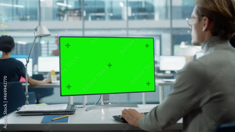 Close Up Over the Shoulder Shot of a Businessman Working on Desktop Computer with Chroma Key Green Screen Mock Up Display. Digital Projects Manager Typing Data, Using Keyboard and Mouse. Close Up Over the Shoulder Shot of a Businessman Working on Desktop Computer with Chroma Key Green Screen Mock Up Display. Digital Projects Manager Typing Data, Using Keyboard and Mouse.