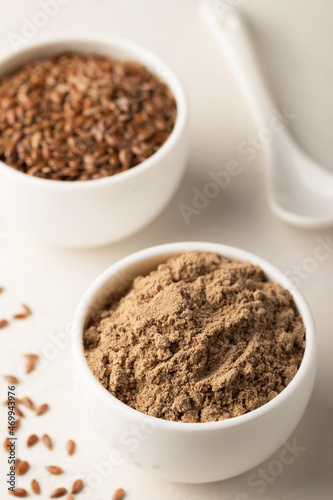 Flaxseed flour in a bowl and flax seeds on a light background. Selective focus. Close-up, copy space