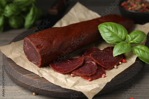 Delicious dry-cured beef basturma with basil and peppercorns on wooden table, closeup photo