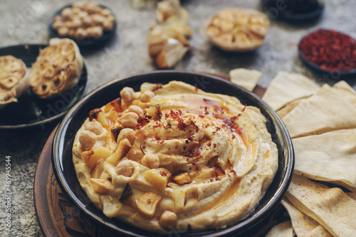 Traditional homemade middle eastern dish - hummus decorated with chickpeas, garlic, olive oil and spices on dark stone table