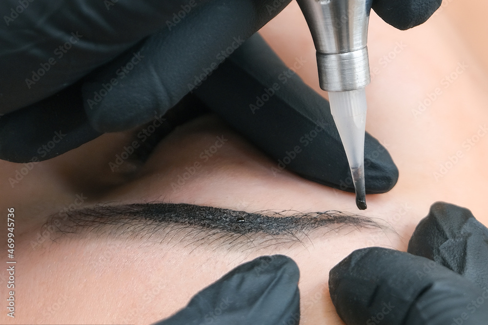 Naklejka premium Beautician makes permanent eyebrow makeup on the face of a beautiful young woman.