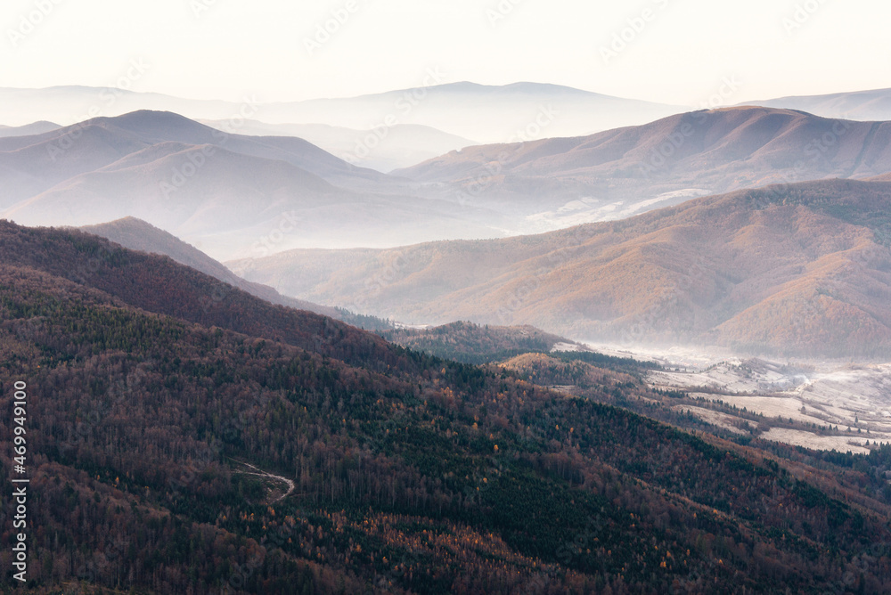 Beautiful landscape of autumn mountains layers range at  hazy morning. A view of the misty slopes of the mountains in the distance and forest hills  in rays of sunlight.Travel nature background.