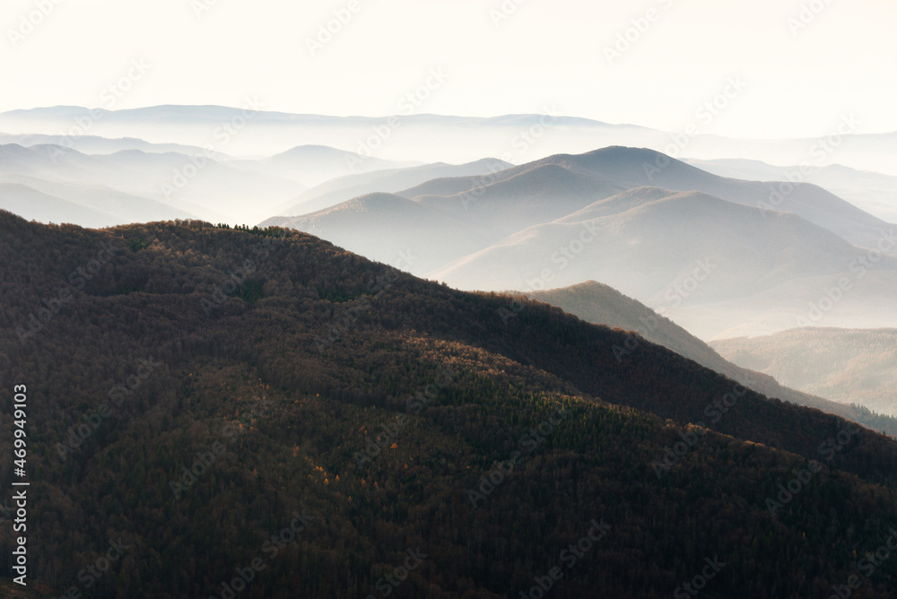 Beautiful landscape of autumn mountains layers range at  hazy morning. A view of the misty slopes of the mountains in the distance and forest hills  in rays of sunlight.Travel nature background.