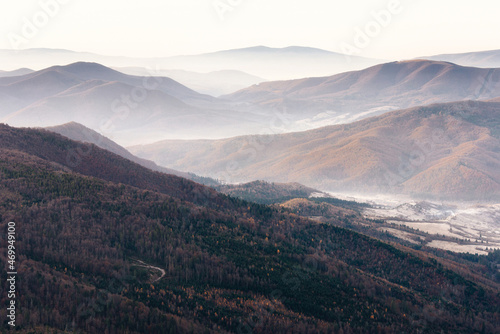 Beautiful landscape of autumn mountains layers range at  hazy morning. A view of the misty slopes of the mountains in the distance and forest hills  in rays of sunlight.Travel nature background. © vovik_mar