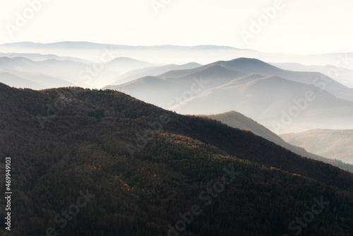 Beautiful landscape of autumn mountains layers range at hazy morning. A view of the misty slopes of the mountains in the distance and forest hills in rays of sunlight.Travel nature background.