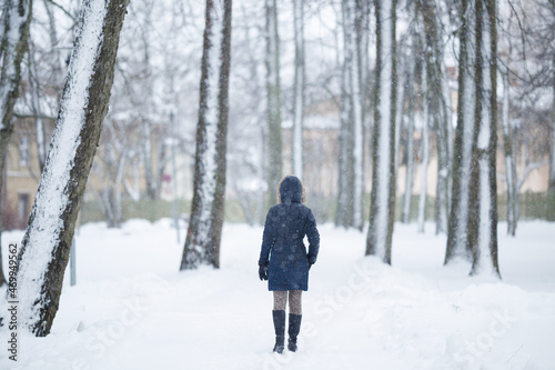 Young adult woman slowly walking through alley of trees in white snowy winter day at park. Fresh first snow. Spending time alone in nature. Peaceful atmosphere. Back view. © fotoduets