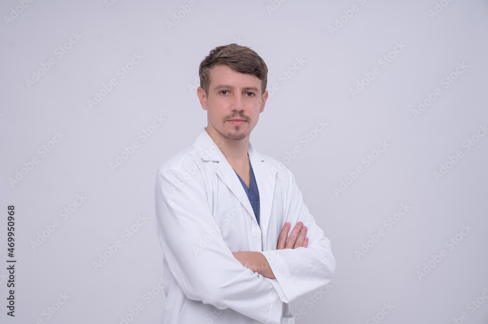 Portrait of young caucasian male medical doctor in white medical gown standing with crossed arms. Isolated on white. Looking at camera with copy space Portrait of young caucasian male medical doctor in white medical gown standing with crossed arms. Isolated on white. Looking at camera with copy space