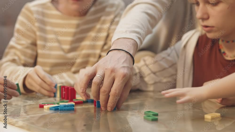 Close-up of cropped people sitting around table and playing colorful childrens dominoes Close-up of cropped people sitting around table and playing colorful childrens dominoes