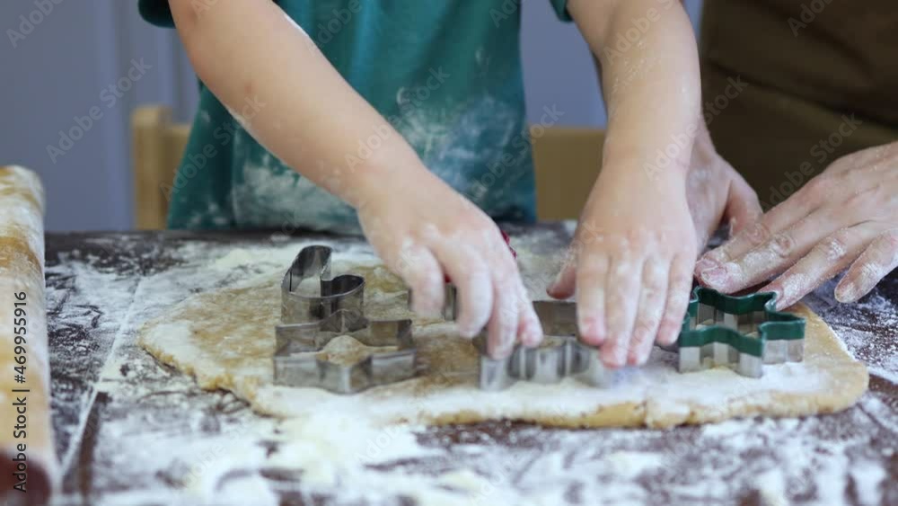 3 year baby boy child cutting star, gingerbread man shape cookies from dough pastry with steel cutters at home kitchen. mother teaching son to make christmas traditional biscuits together. table flour