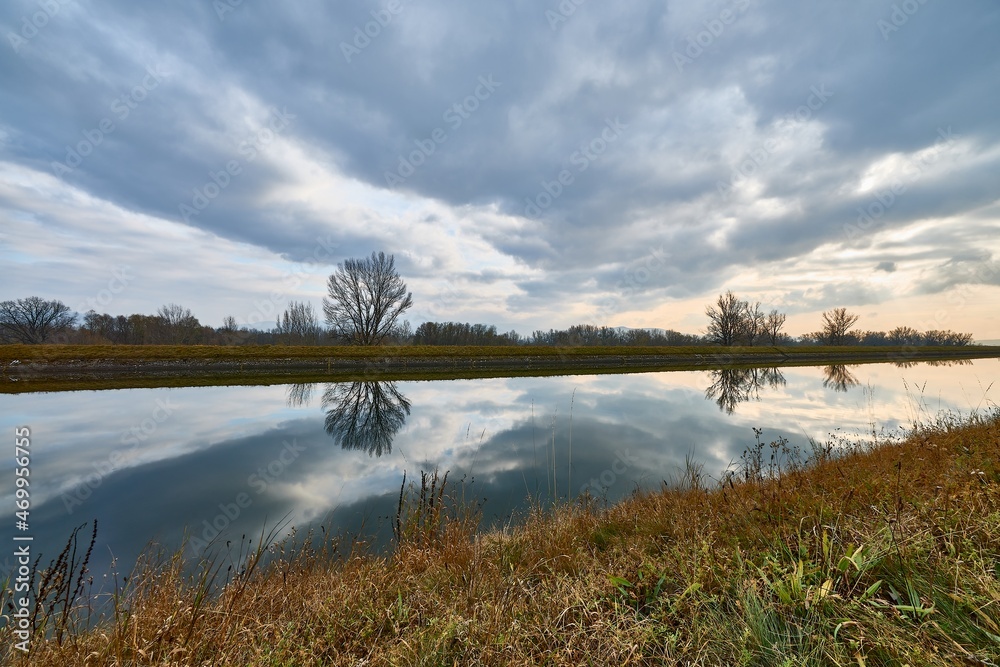 Autumn cloudy day with dramatic sky. Landscape with waterway and reflections of clouds on the water surface.  Trencin, Slovakia.