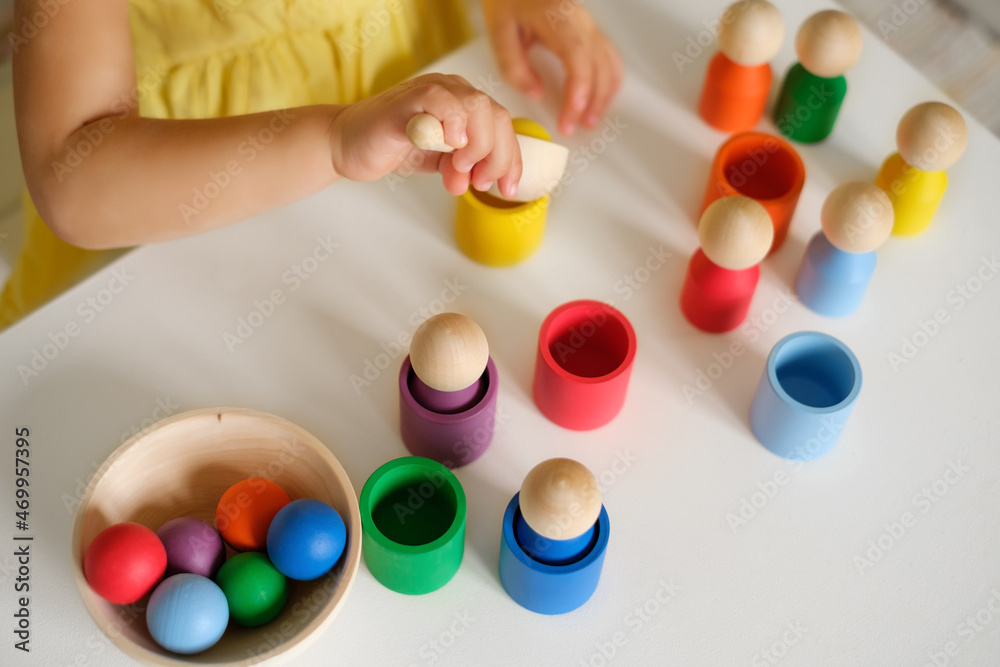 Child throws a yellow ball into a cup of the appropriate color with a spoon. Educational game - sort figures by colors. Wooden Multicolored Developmental Toy for Preschoolers Child throws a yellow ball into a cup of the appropriate color with a spoon. Educational game - sort figures by colors. Wooden Multicolored Developmental Toy for Preschoolers