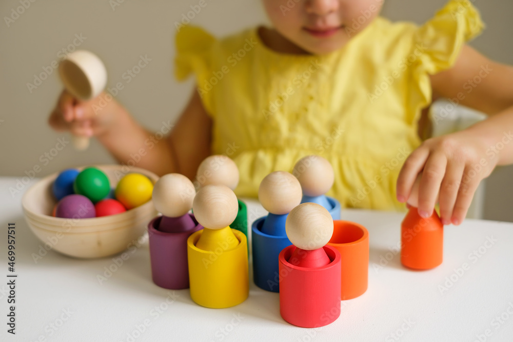 Obraz premium Wooden colored toy for learning colors and developing logic of preschoolers. A child plays at a table in the children's room with cups, balls and cylinders. Preschool education