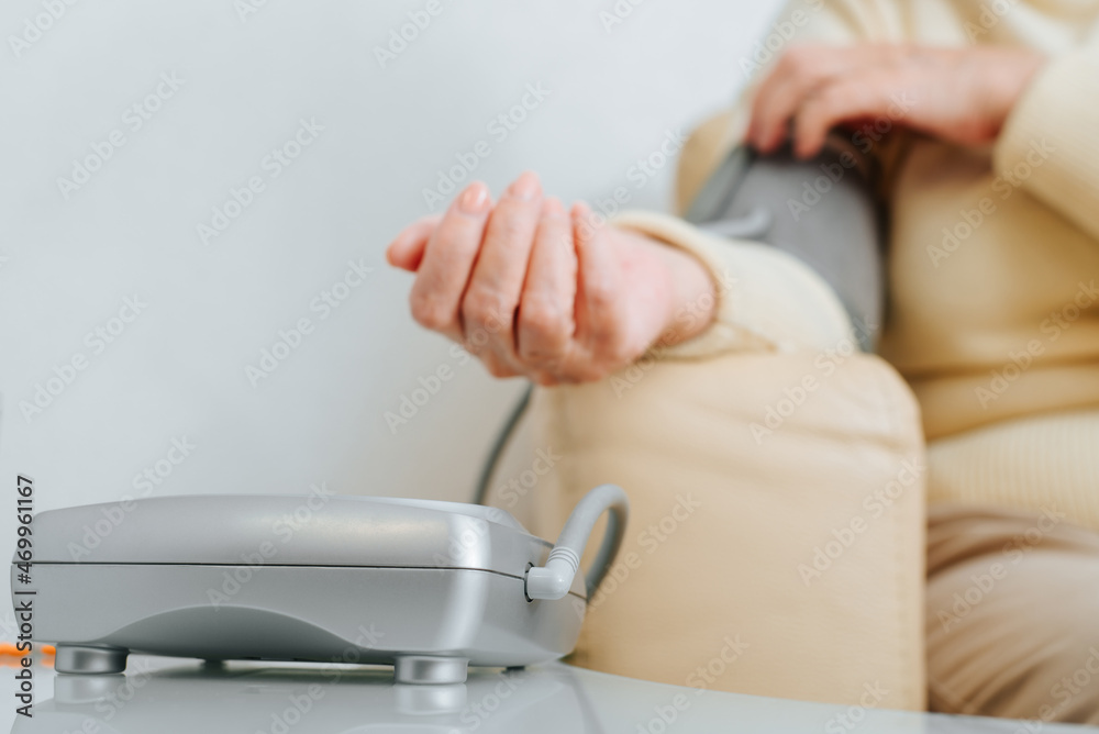 Close-up of senior sick woman checking her blood pressure and pulse indoors. Selective focus on tanometer, medical measuring instrument. Hypertension, elderly and healthcare
