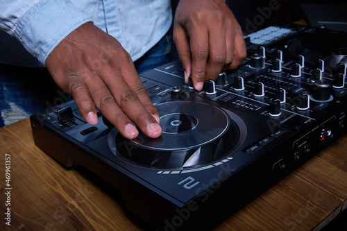 Producer working in music record studio. There is a mixer on a wooden table and an black man creates music on it.