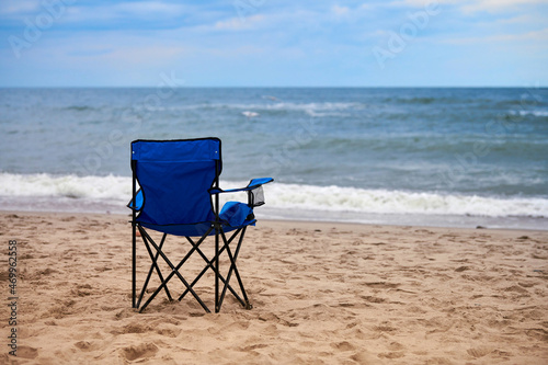 Fototapeta Naklejka Na Ścianę i Meble -  Blue folding chair back on sea beach, without people, beach holiday alone, loneliness