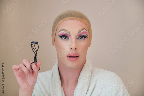 Konstfotografi Drag queen person with a eyelash curler and wearing bathrobe looking at camera