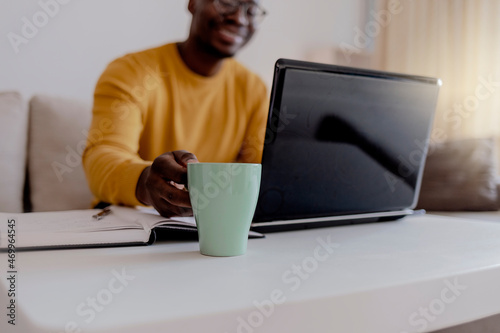 Cropped shot of a handsome young businessman sitting alone in his home office and working on laptop computer at home. Smiling black man using laptop in living room. Businessman using laptop at home.