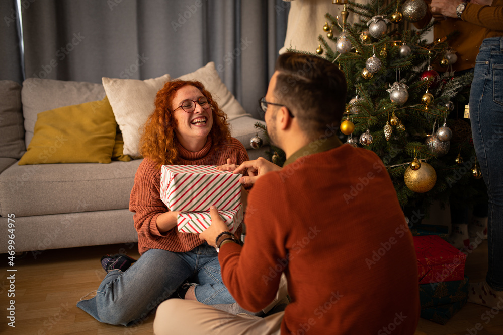 Young couple in love sitting on a sofa next to a Christmas tree. The guy gives the woman a gift for the new year Young couple in love sitting on a sofa next to a Christmas tree. The guy gives the woman a gift for the new year