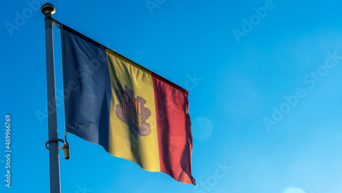 National flag of Andorra on a flagpole in front of blue sky with sun rays and lens flare. Diplomacy concept.
